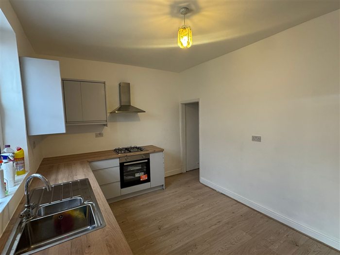 Same room after: new kitchen along one wall, white walls and wood-effect floor